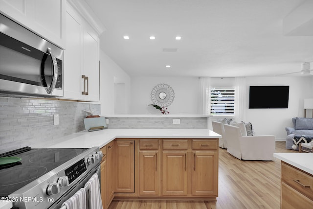 kitchen with open floor plan, stainless steel appliances, light wood-style floors, a peninsula, and light countertops