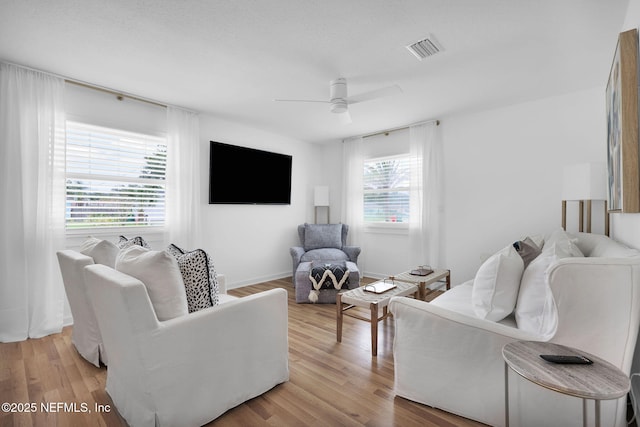 living room with visible vents, baseboards, light wood-style floors, and a ceiling fan