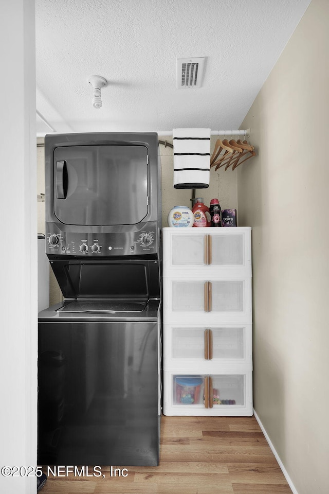 laundry room featuring visible vents, a textured ceiling, wood finished floors, stacked washing maching and dryer, and laundry area