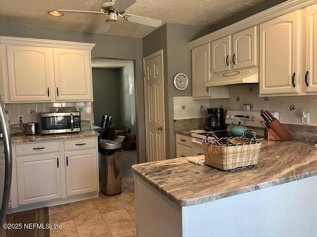 kitchen with stainless steel microwave, backsplash, a ceiling fan, white range with gas cooktop, and under cabinet range hood