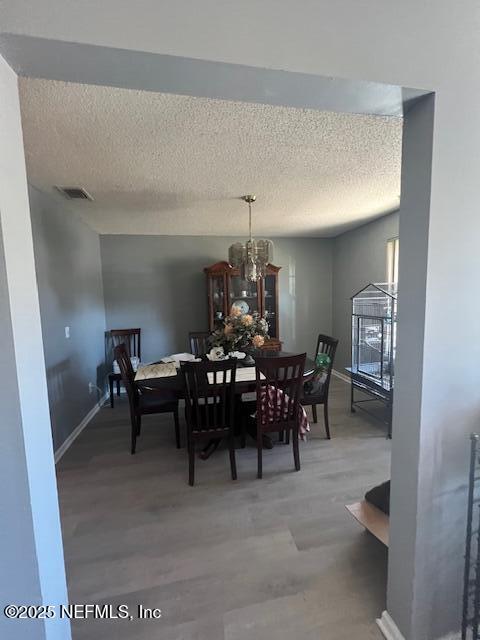 dining room featuring a textured ceiling, wood finished floors, visible vents, and baseboards