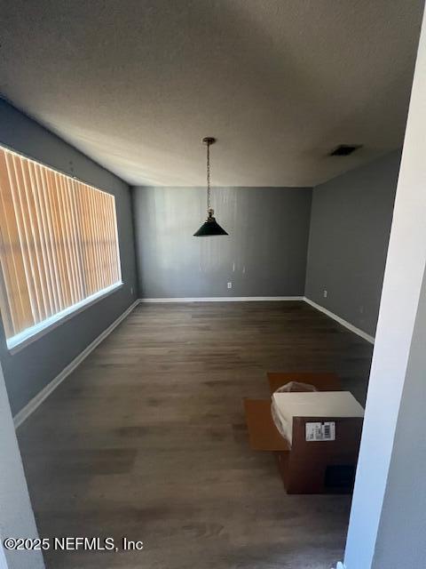 unfurnished dining area featuring visible vents, a textured ceiling, baseboards, and wood finished floors