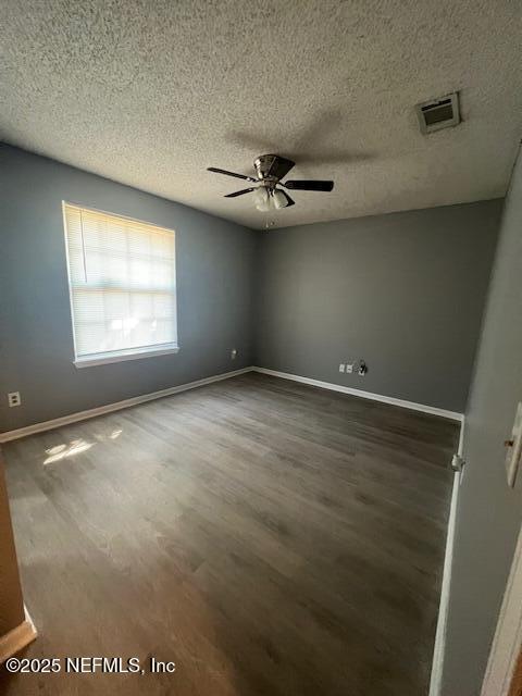 empty room with ceiling fan, a textured ceiling, wood finished floors, visible vents, and baseboards