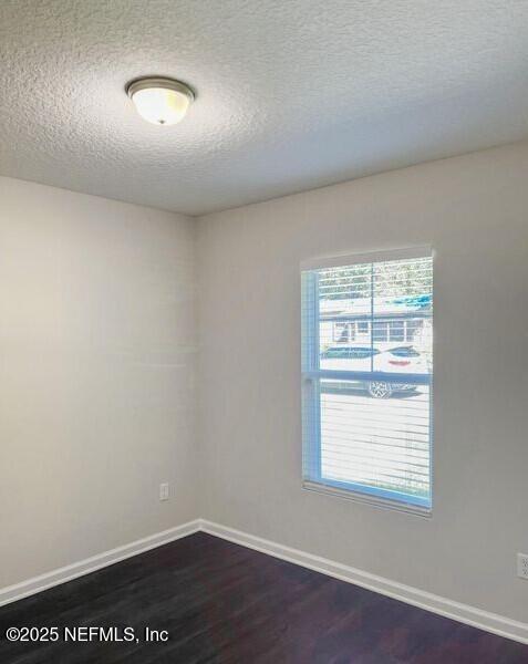 spare room featuring dark wood-style flooring, a textured ceiling, and baseboards