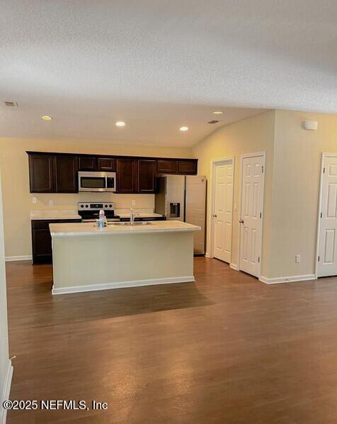 kitchen featuring appliances with stainless steel finishes, light countertops, an island with sink, and dark wood-style floors