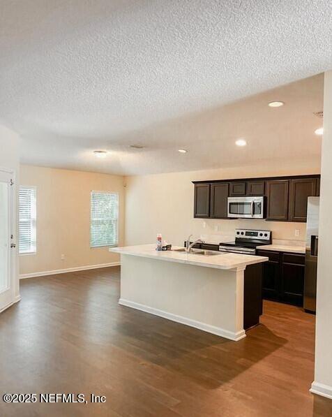 kitchen with stainless steel appliances, dark wood-type flooring, a sink, and a kitchen island with sink