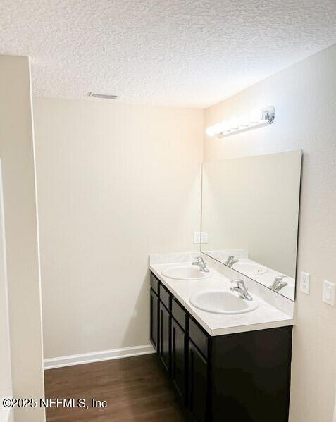 full bath with double vanity, a textured ceiling, a sink, and wood finished floors