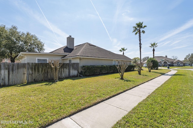 view of home's exterior with a lawn, a chimney, fence, and stucco siding