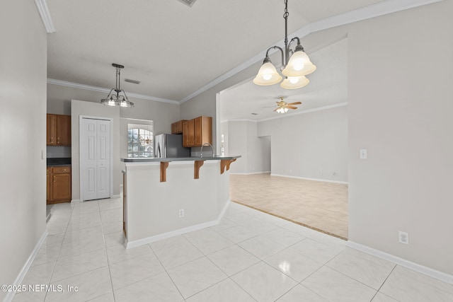 kitchen featuring brown cabinets, a breakfast bar, freestanding refrigerator, crown molding, and ceiling fan with notable chandelier