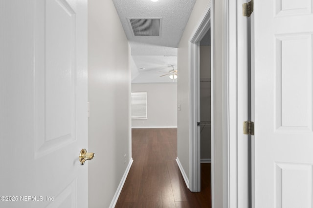 hallway featuring dark wood-style flooring, visible vents, a textured ceiling, and baseboards