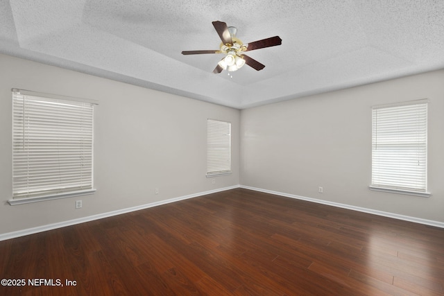 unfurnished room featuring dark wood finished floors, a raised ceiling, a ceiling fan, a textured ceiling, and baseboards