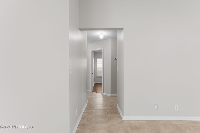 corridor with baseboards, a textured ceiling, and light tile patterned flooring