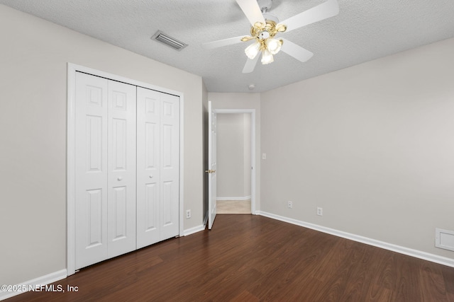 unfurnished bedroom featuring dark wood-style flooring, a closet, visible vents, a textured ceiling, and baseboards