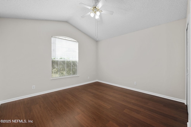 spare room featuring baseboards, a ceiling fan, dark wood-style flooring, vaulted ceiling, and a textured ceiling