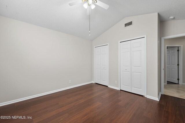 unfurnished bedroom featuring dark wood-style flooring, two closets, visible vents, vaulted ceiling, and baseboards