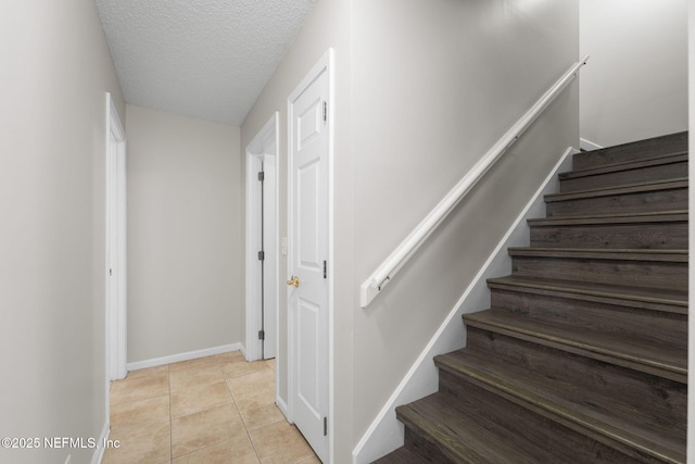 stairs featuring tile patterned flooring, a textured ceiling, and baseboards