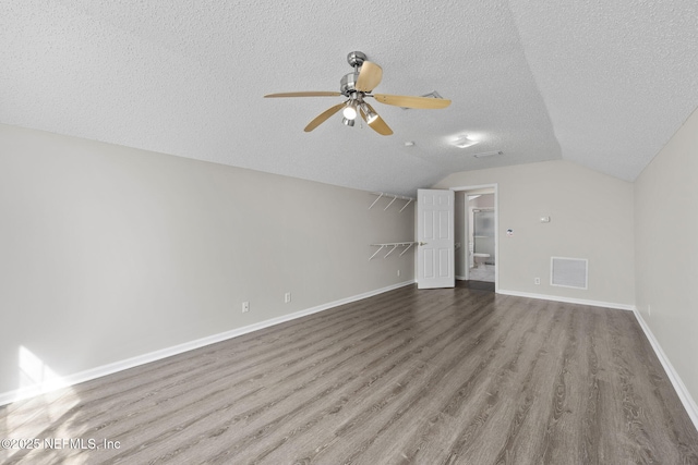 interior space with a textured ceiling, wood finished floors, visible vents, baseboards, and vaulted ceiling