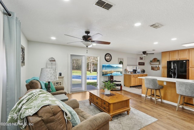 living room featuring a textured ceiling, visible vents, and light wood-style floors