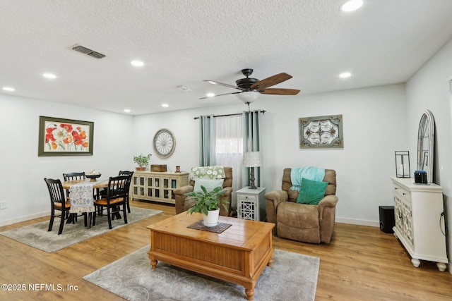 living area with a textured ceiling, light wood finished floors, visible vents, and recessed lighting