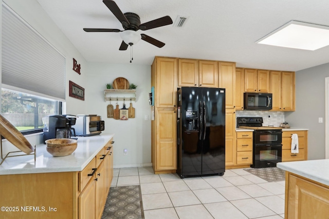 kitchen with light tile patterned flooring, a skylight, light countertops, black appliances, and tasteful backsplash