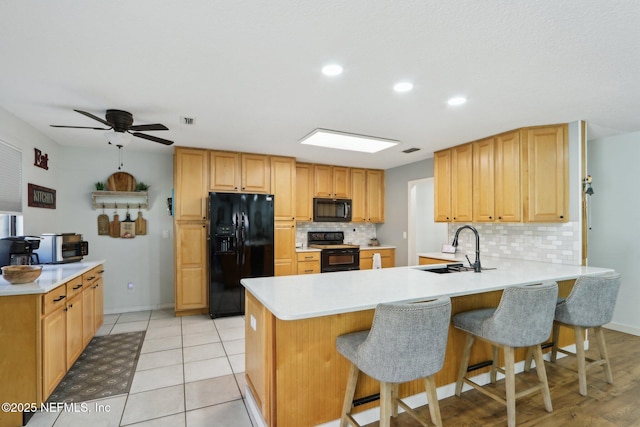 kitchen with light countertops, a sink, a peninsula, and black appliances