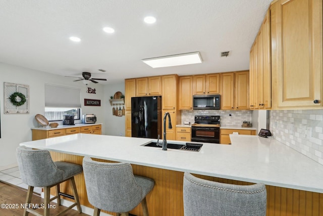 kitchen with a peninsula, a sink, visible vents, black appliances, and tasteful backsplash