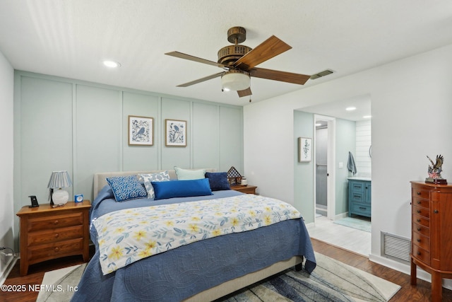 bedroom featuring a ceiling fan, visible vents, a decorative wall, and wood finished floors