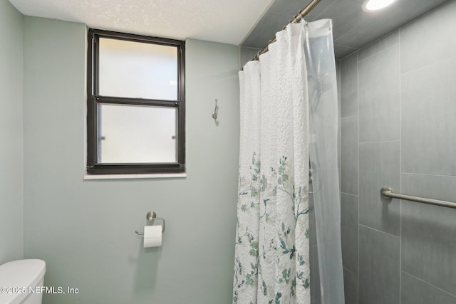 bathroom featuring toilet, a tile shower, and a textured ceiling