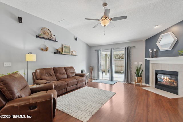 living area featuring lofted ceiling, ceiling fan, a tile fireplace, and wood finished floors