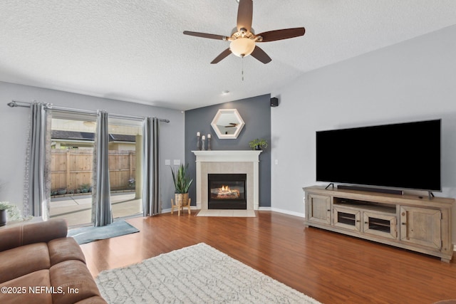 living room featuring a textured ceiling, ceiling fan, a fireplace, wood finished floors, and baseboards