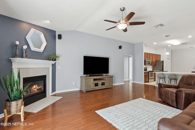 living room with visible vents, baseboards, a ceiling fan, a tiled fireplace, and light wood-style floors