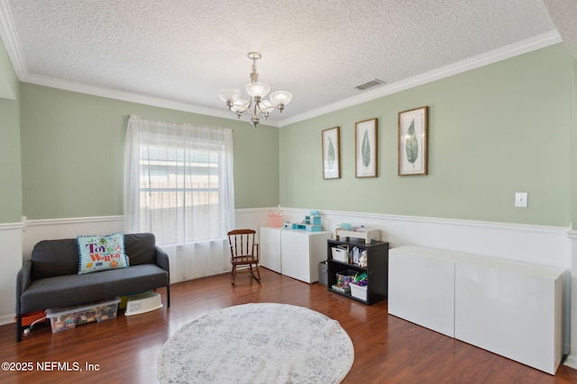 living area with a textured ceiling, a notable chandelier, wood finished floors, visible vents, and crown molding