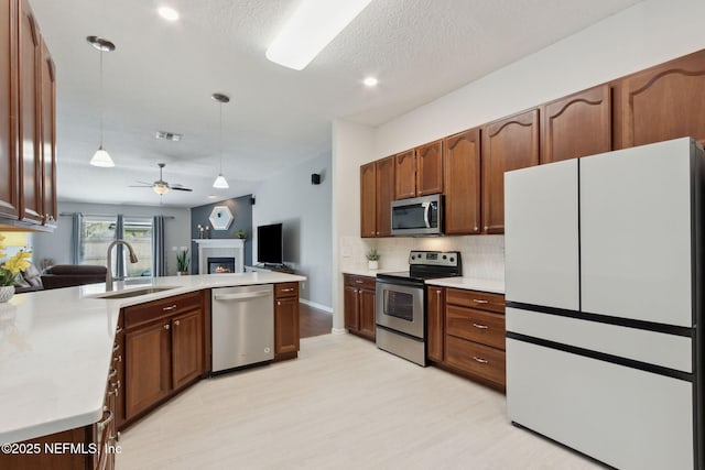 kitchen featuring pendant lighting, stainless steel appliances, light countertops, a sink, and a peninsula