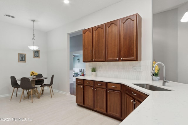 kitchen featuring decorative light fixtures, visible vents, light countertops, backsplash, and a sink