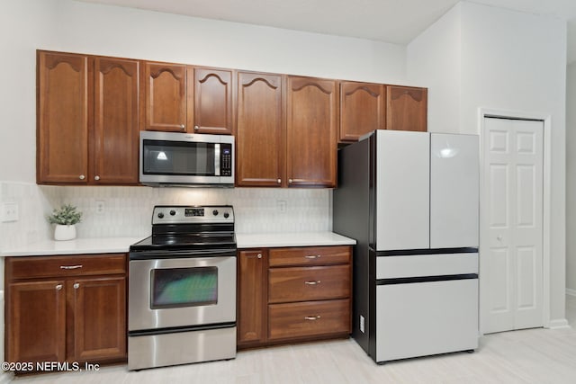 kitchen with brown cabinets, tasteful backsplash, appliances with stainless steel finishes, and light countertops