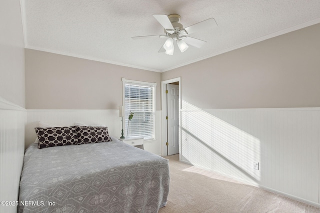 carpeted bedroom with a wainscoted wall, ornamental molding, and a textured ceiling