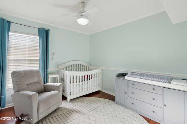 bedroom with a crib, baseboards, a ceiling fan, wood finished floors, and crown molding