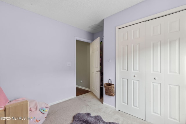 carpeted bedroom featuring a textured ceiling, a closet, and baseboards