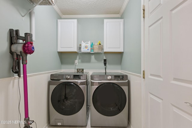 clothes washing area featuring a textured ceiling, ornamental molding, wainscoting, cabinet space, and washing machine and clothes dryer