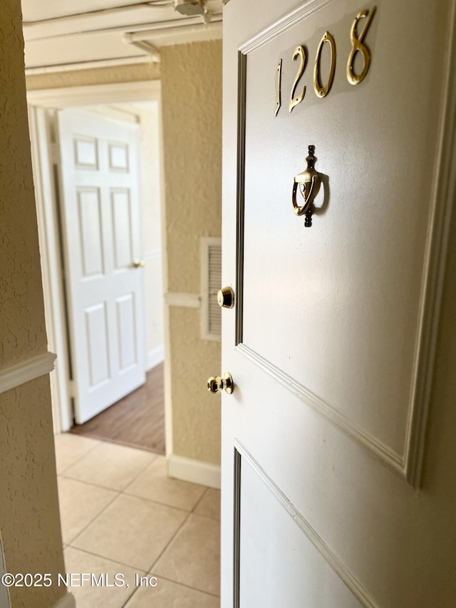 hall featuring light tile patterned floors, visible vents, and a textured wall