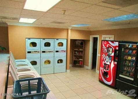 recreation room with stacked washer and clothes dryer, a drop ceiling, and light tile patterned flooring