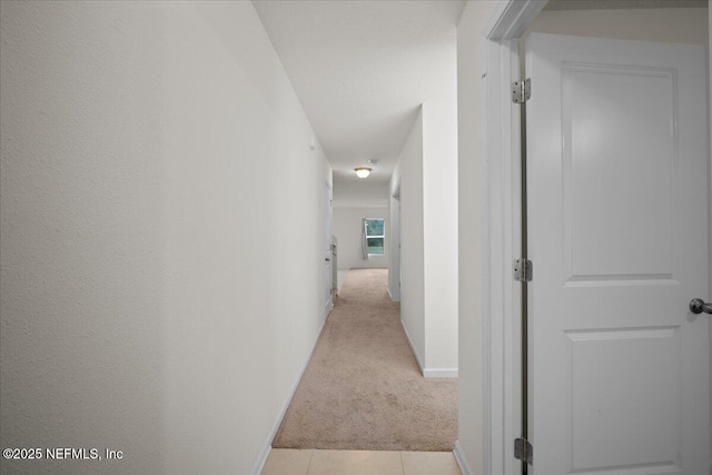 hall with baseboards, light tile patterned floors, and light colored carpet