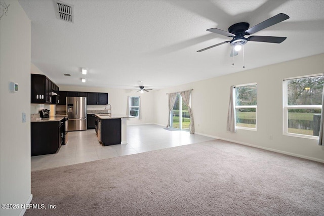 kitchen featuring visible vents, open floor plan, light carpet, a sink, and stainless steel fridge