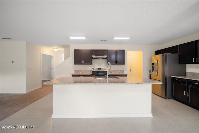 kitchen featuring light stone counters, under cabinet range hood, a sink, appliances with stainless steel finishes, and a center island with sink