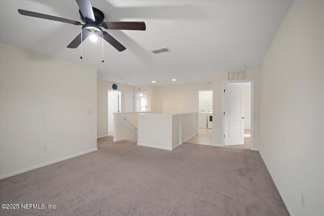 spare room featuring a textured ceiling, light carpet, washing machine and clothes dryer, and visible vents