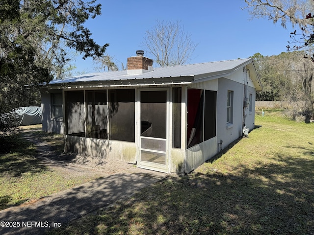 rear view of property featuring a sunroom, a lawn, a chimney, and metal roof