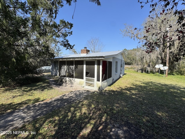 rear view of house with a sunroom, a chimney, metal roof, and a lawn