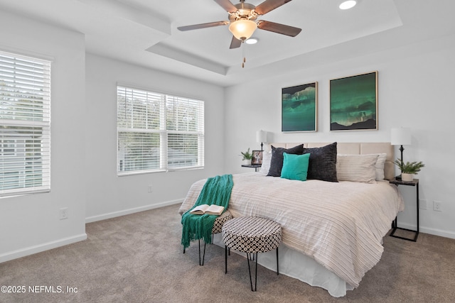 carpeted bedroom featuring baseboards, a raised ceiling, and a ceiling fan