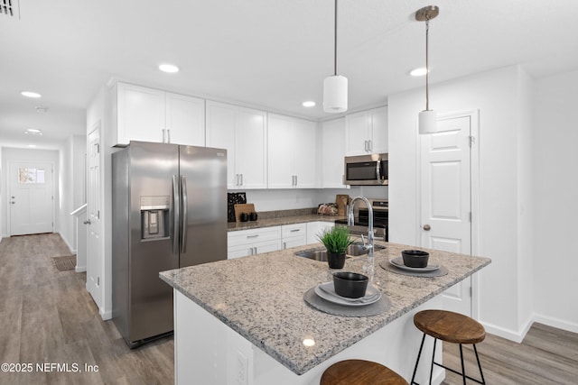 kitchen with light wood finished floors, appliances with stainless steel finishes, white cabinetry, a sink, and light stone countertops