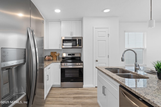 kitchen with appliances with stainless steel finishes, light stone countertops, light wood-style floors, white cabinetry, and a sink